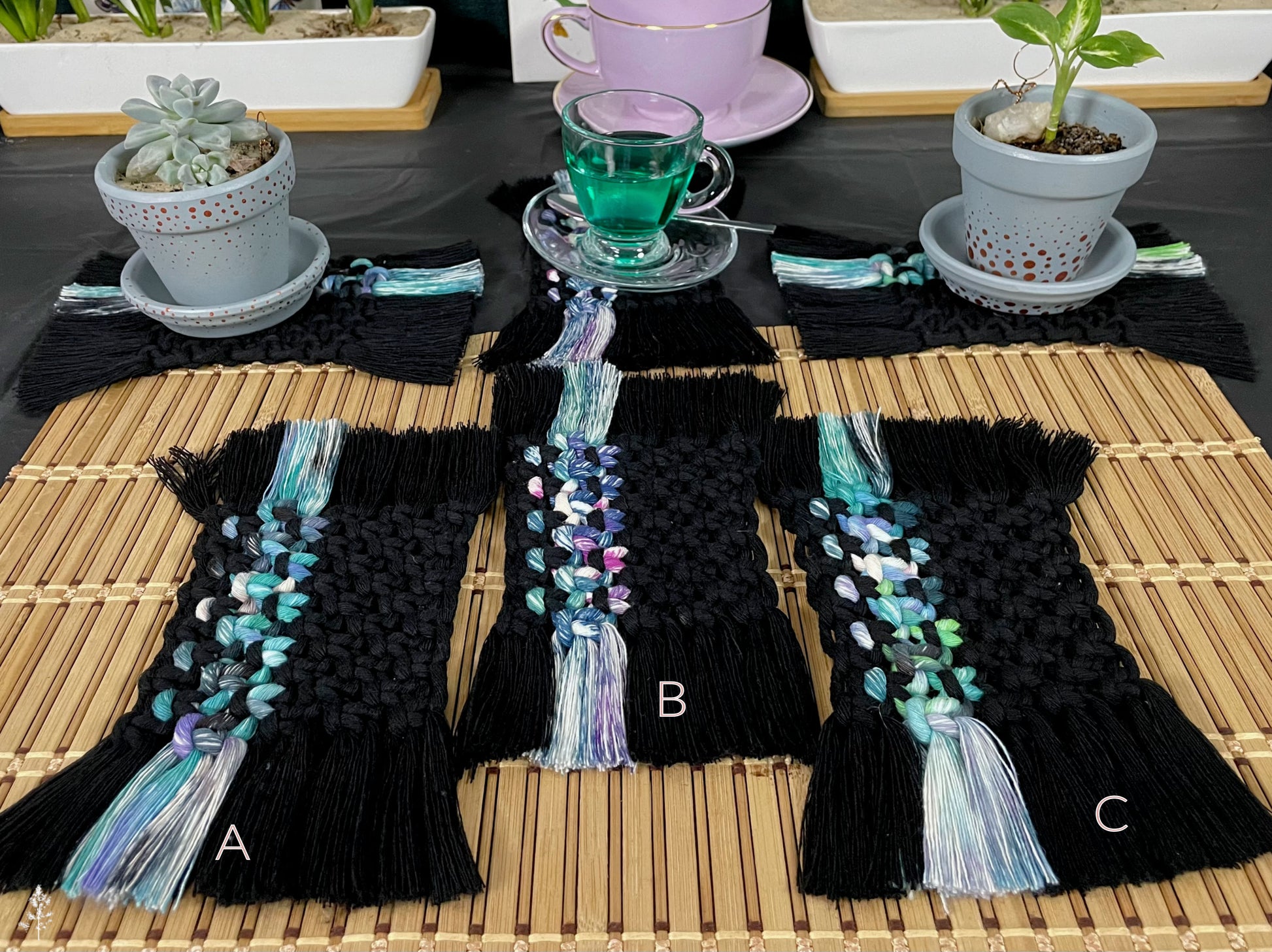 Black macrame coasters with colorful tassels on a wooden table with plants and tea set.
