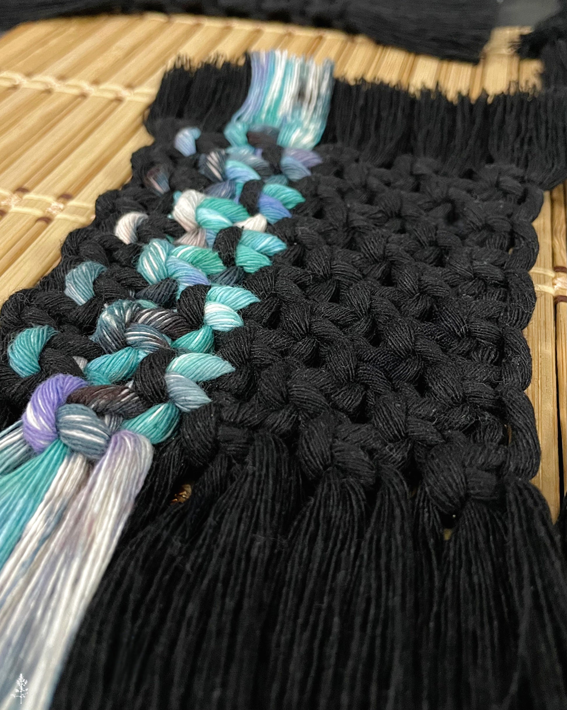 Close-up of a black macrame coaster with colorful fringe on a wooden surface.