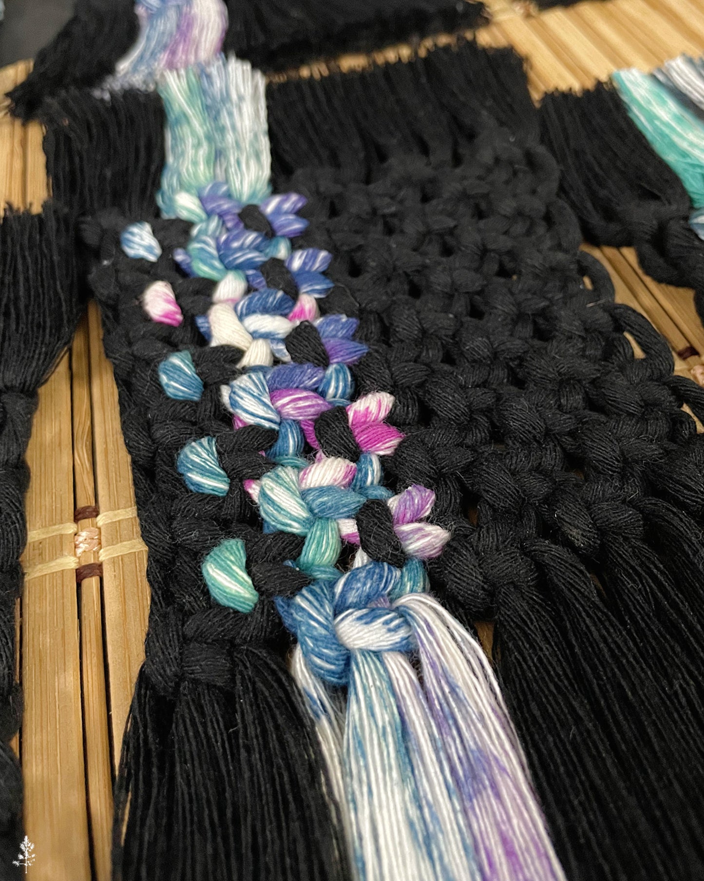 Black macrame coaster with colorful tassels on a wooden surface