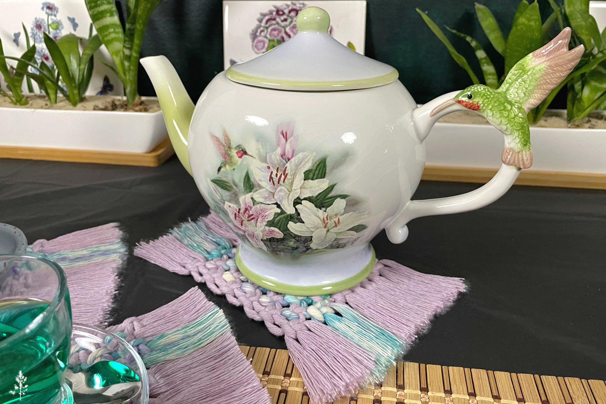 Ceramic teapot with floral design on a table with a glass of water and decorative elements.